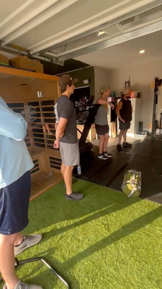 Guys standing by the sauna and curved treadmill inside the garage