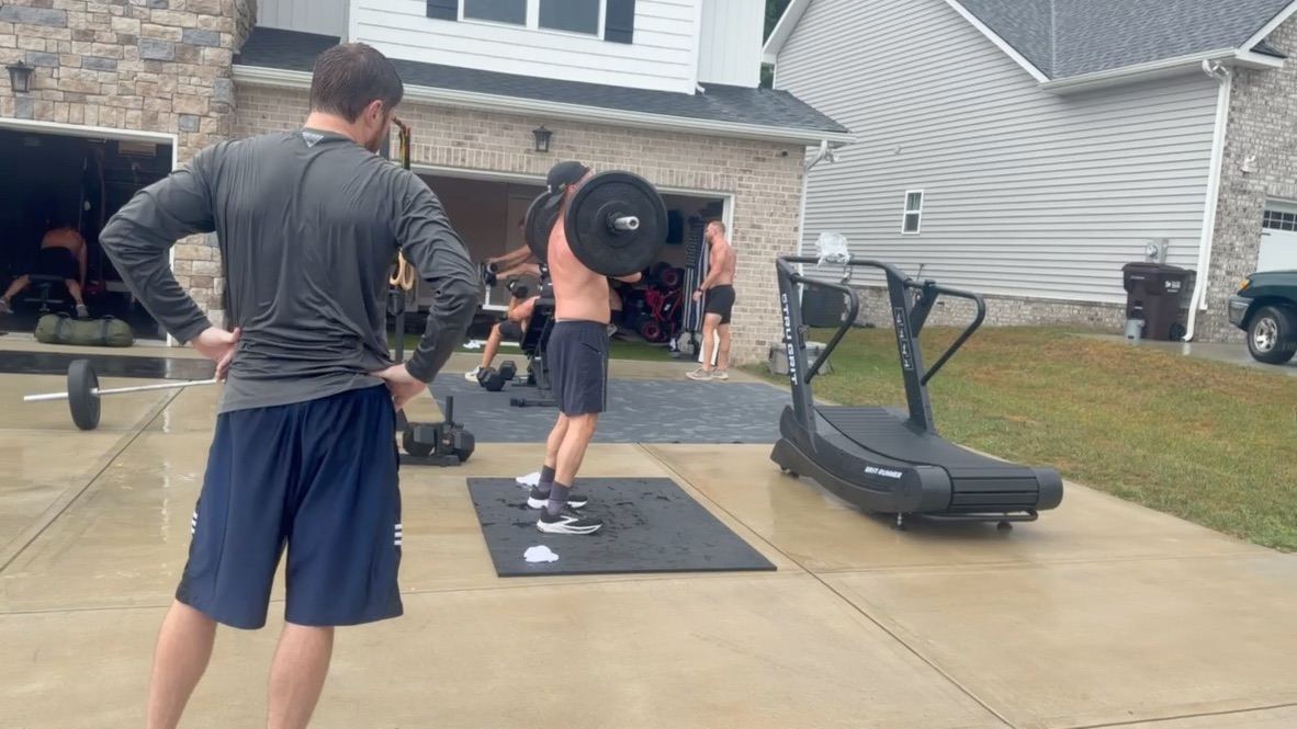Front-racking a barbell in the driveway beside the curved treadmill
